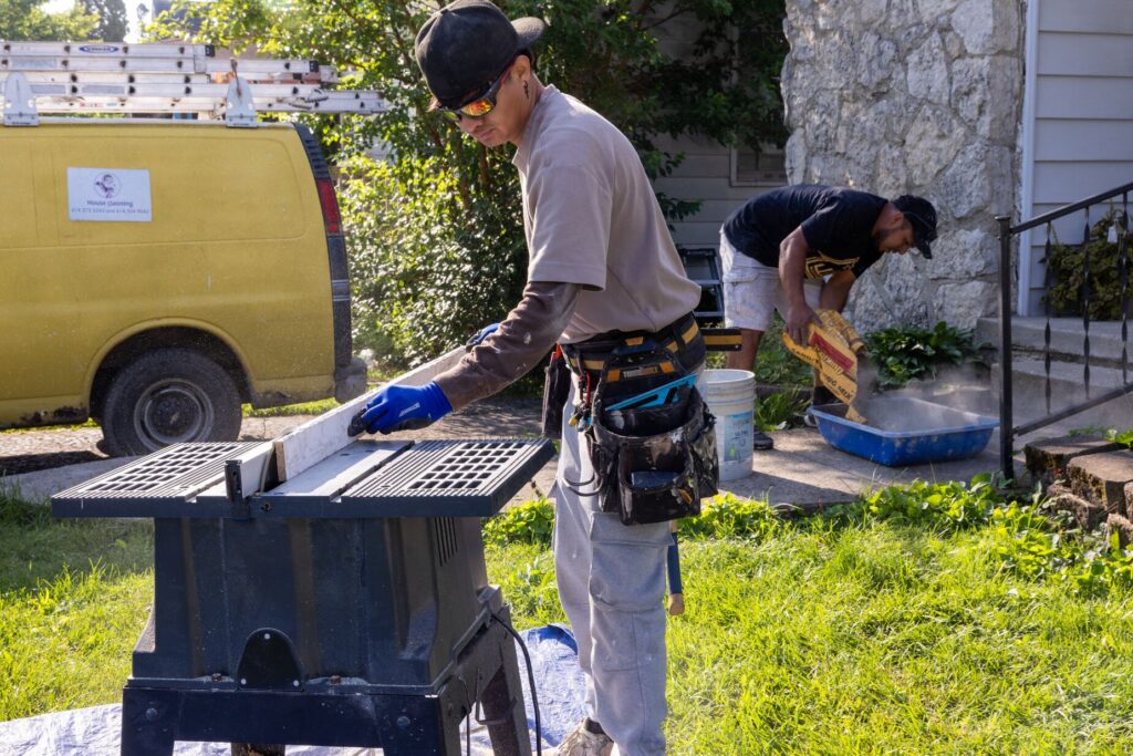 man cutting wall and another man pouring concrete into a bin as they repair a home